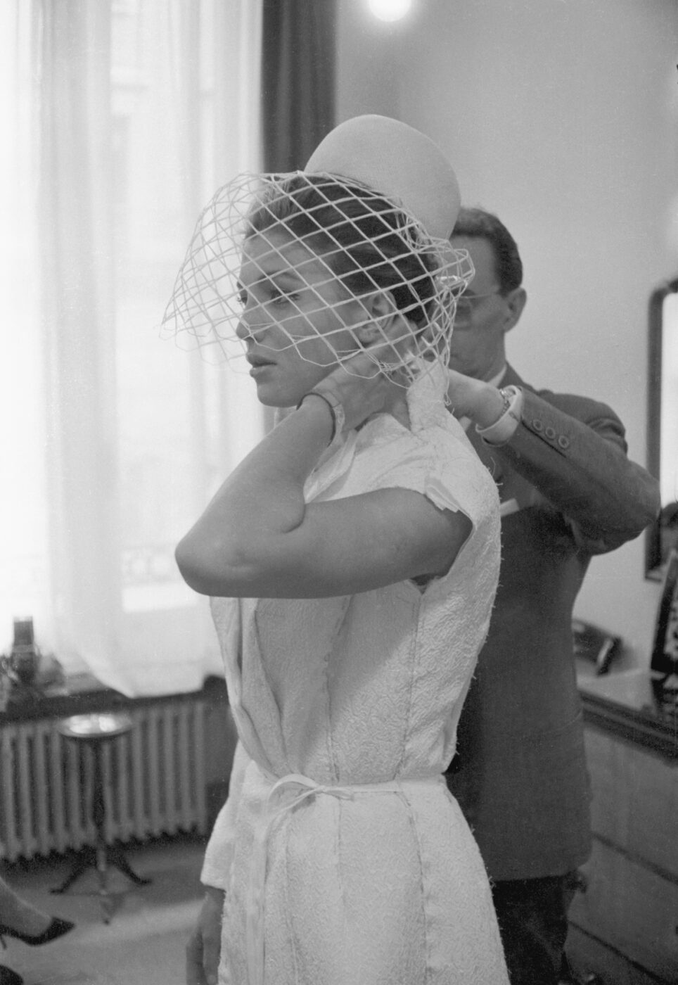 Photographic Social Vision - El hijo del modista Pedro Rodríguez en el atelier madrileño probando el traje de novia a Carmen Cervera para su boda con Lex Barker, Madrid, 1964