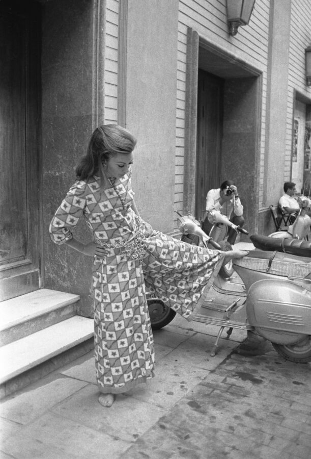 Photographic Social Vision - Lourdes Albert con un traje pantalón de la boutique Hit Parade, con el periodista Jean Michel Bamberger, marido de Joana Biarnés, al fondo, Granada, 1967